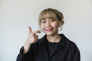 Asian woman smiling while signing in American Sign Language against a neutral background.